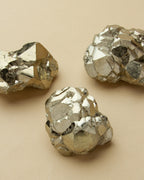 Three pyrite nuggets are displayed against a tan background.