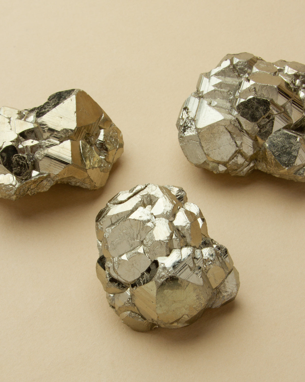 Three pyrite nuggets are displayed against a tan background.