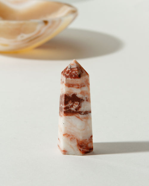 Beige Amplify Calcite Gemstone Mini Tower with reddish-brown bands on a white table.
