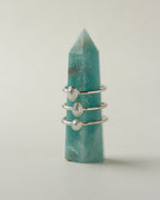 Sand to Stone Freshwater Pearl Rings in oval, teardrop and round shapes, stacked on a blue gemstone.