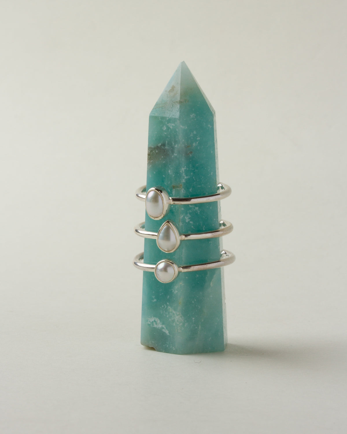 Sand to Stone Freshwater Pearl Rings in oval, teardrop and round shapes, stacked on a blue gemstone.