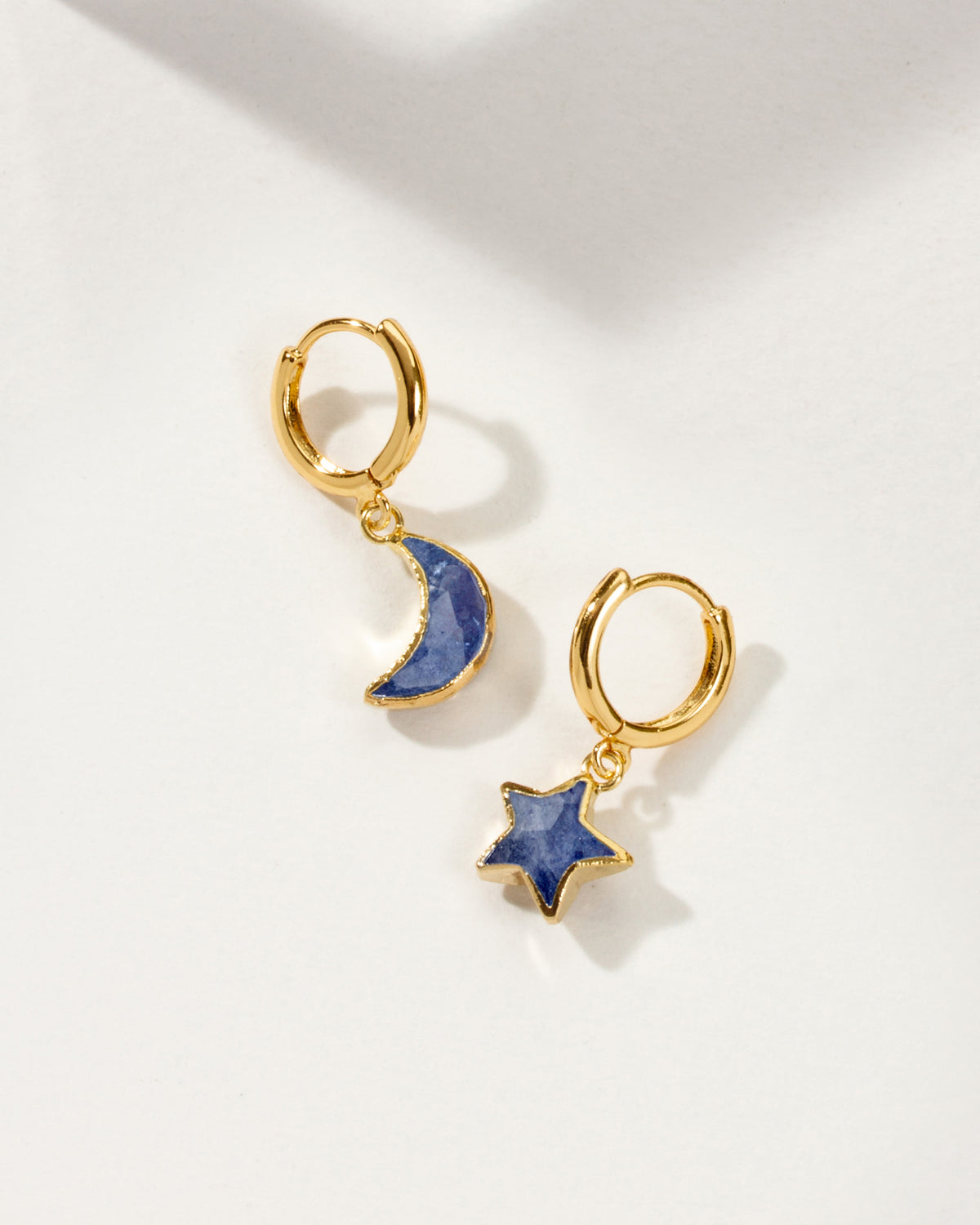 Pair of mismatched gold huggie hoop earrings with sapphire star and moon charms