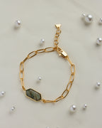 Gold chain bracelet featuring a gleaming labradorite gemstone on a light fabric with pearl accents.