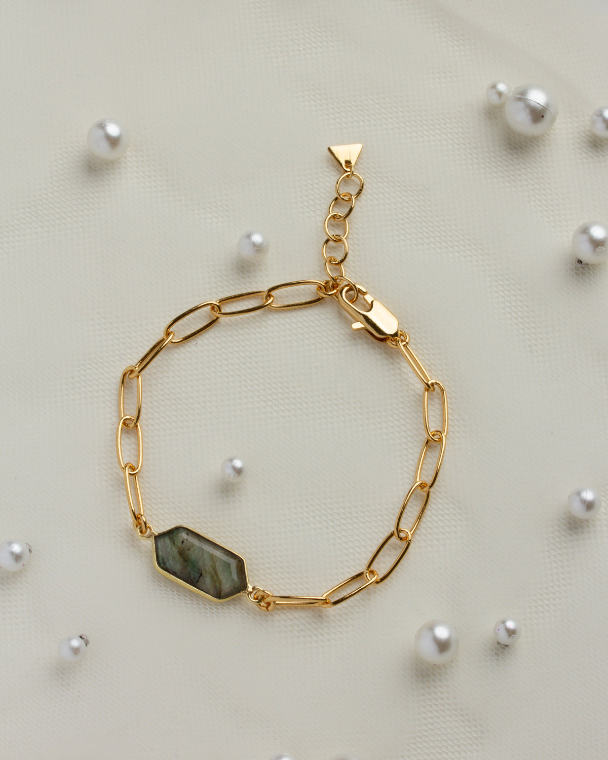 Gold chain bracelet featuring a gleaming labradorite gemstone on a light fabric with pearl accents.