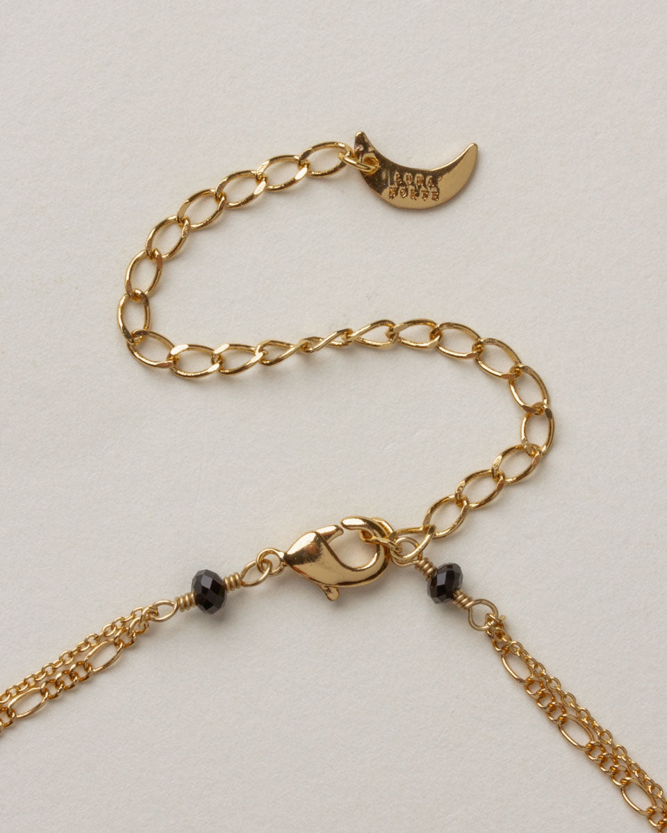 Gold chain and clasp, with black beads and moon-shaped charm on the Spellbound Layered Necklace.