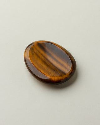 A smooth tiger's eye stone with a slight indent, placed on a white surface.