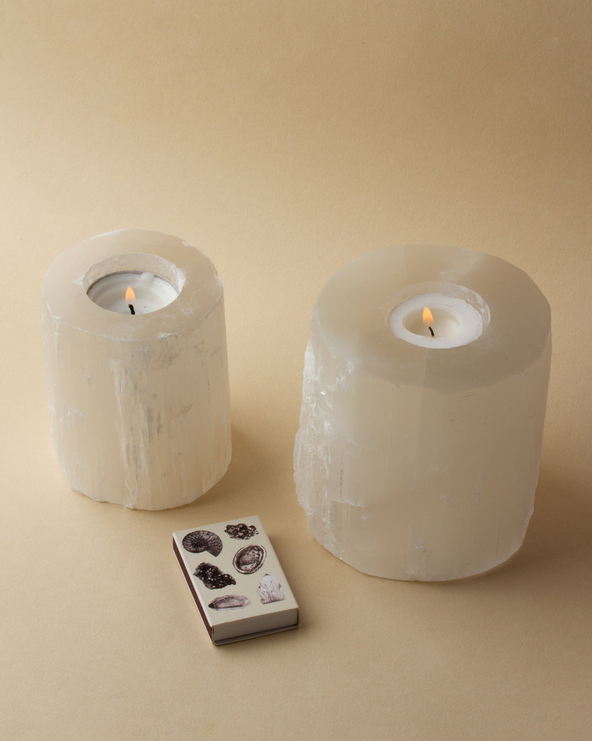 Two lit Tranquility Candle Holders sit next to a matchbox with images of minerals.