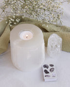 Selenite candle holder with lit candle, quartz crystal, mineral matches, and baby's breath