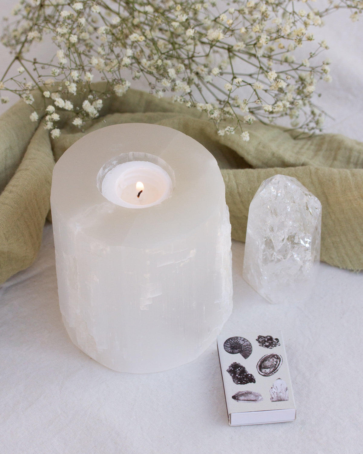 Selenite candle holder with lit candle, quartz crystal, mineral matches, and baby's breath