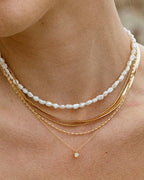 Woman wearing layered gold necklace with pearl strand and opal pendant