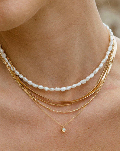 Woman wearing layered gold necklace with pearl strand and opal pendant