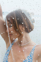 Woman wearing the Orb Front Back Earring in Gold with a floral print top and layered necklaces.