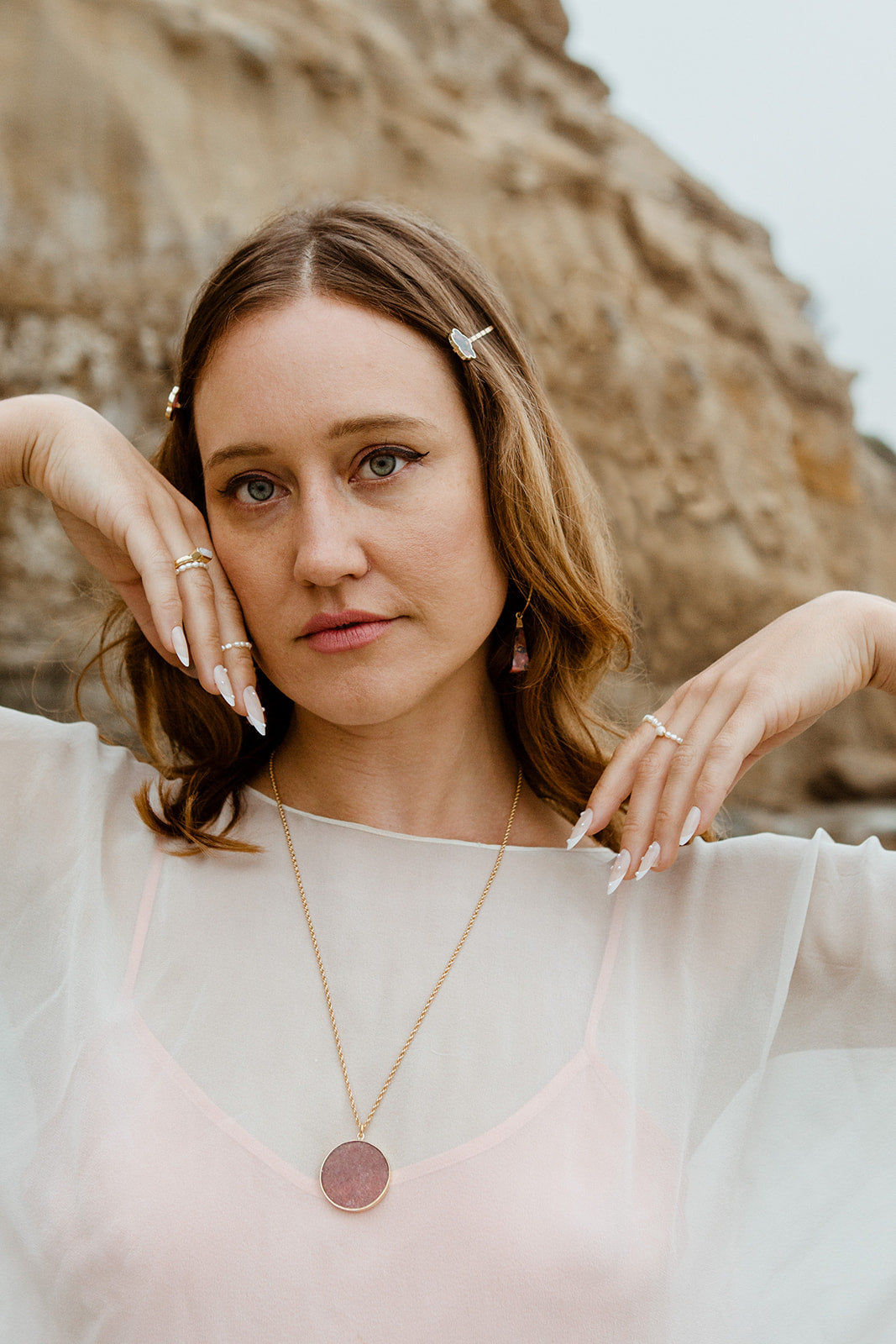 A woman wears the Strawberry Moon Medallion Necklace with a gold chain and pink quartz pendant.